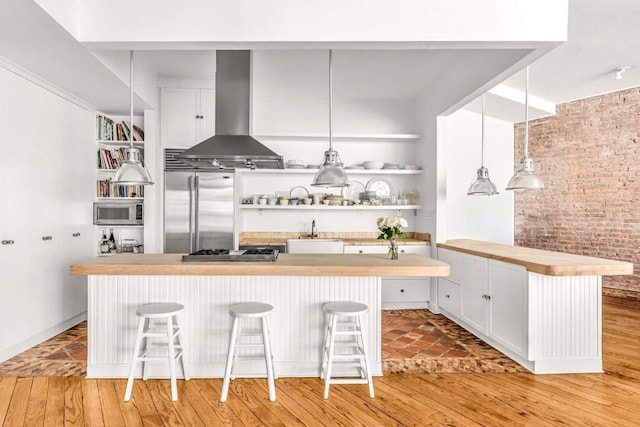 kitchen featuring a breakfast bar, built in appliances, hanging light fixtures, island exhaust hood, and white cabinets