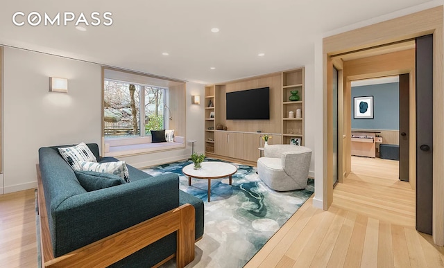 living room with built in shelves, baseboards, and light wood finished floors