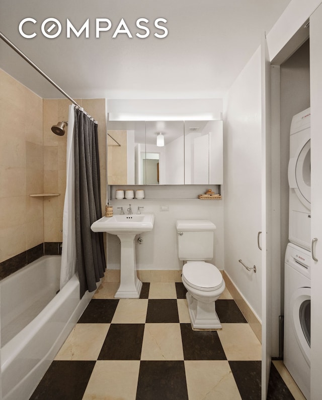 full bath featuring toilet, stacked washer and dryer, baseboards, tile patterned floors, and shower / bath combo