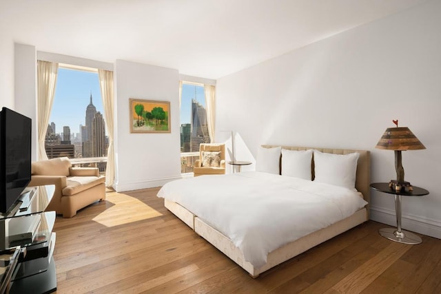 bedroom featuring a view of city, light wood-style flooring, and baseboards