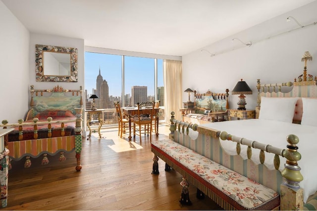 bedroom featuring a view of city, a wall of windows, and wood finished floors