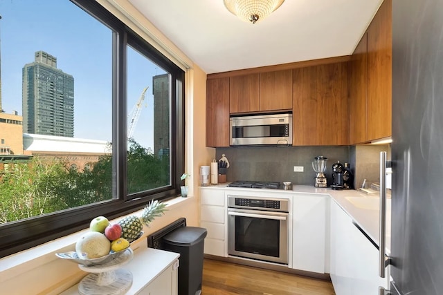 kitchen with backsplash, white cabinetry, appliances with stainless steel finishes, and light hardwood / wood-style flooring