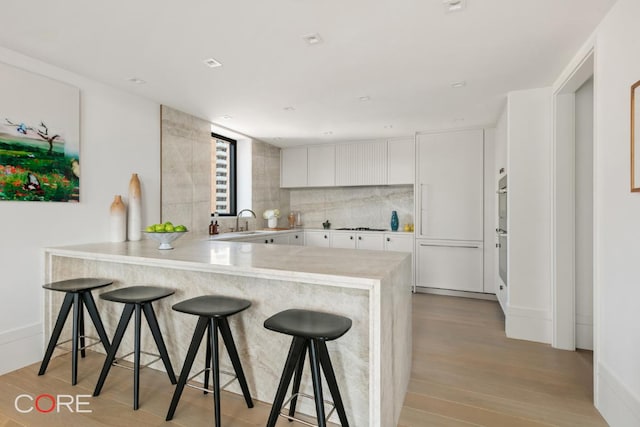 kitchen featuring sink, white cabinets, a kitchen breakfast bar, light hardwood / wood-style floors, and kitchen peninsula