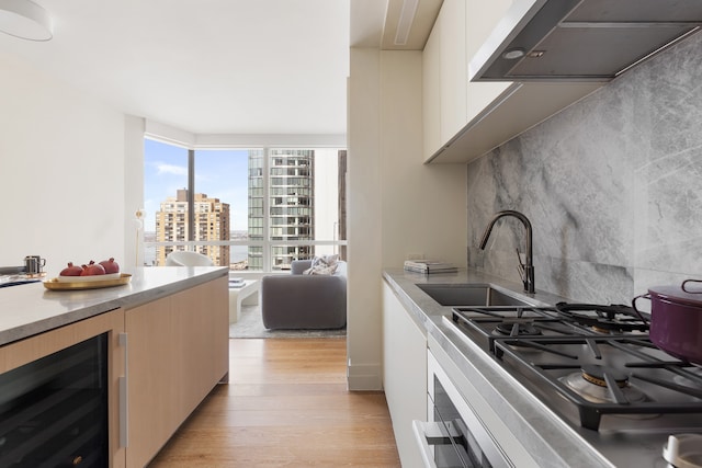 kitchen with wine cooler, range hood, a view of city, light wood-style floors, and a sink