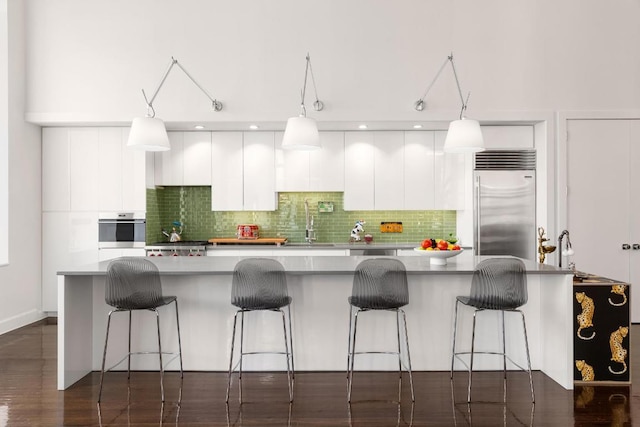 kitchen featuring a center island with sink, hanging light fixtures, appliances with stainless steel finishes, decorative backsplash, and white cabinets