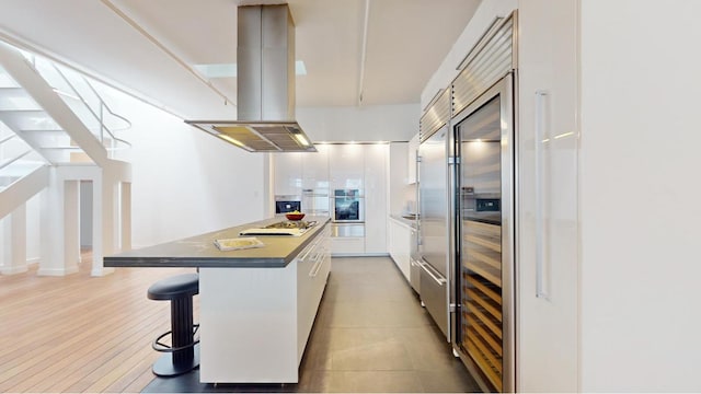 kitchen featuring stainless steel appliances, a center island, island range hood, white cabinets, and a kitchen bar