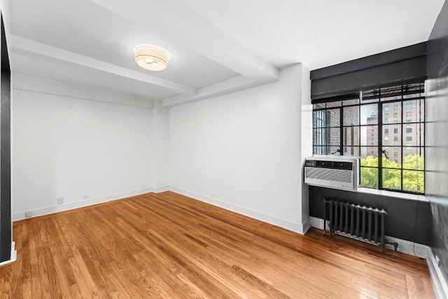 empty room with cooling unit, radiator heating unit, and wood-type flooring