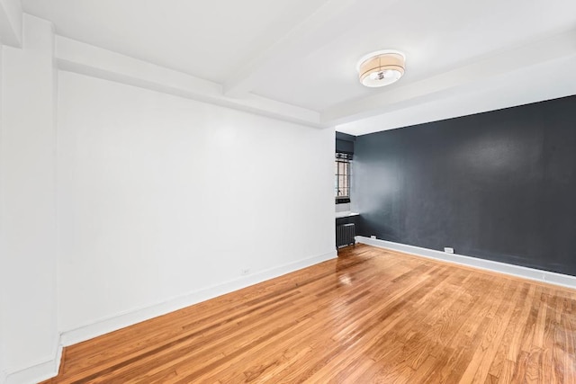 empty room featuring hardwood / wood-style flooring, radiator heating unit, and beam ceiling