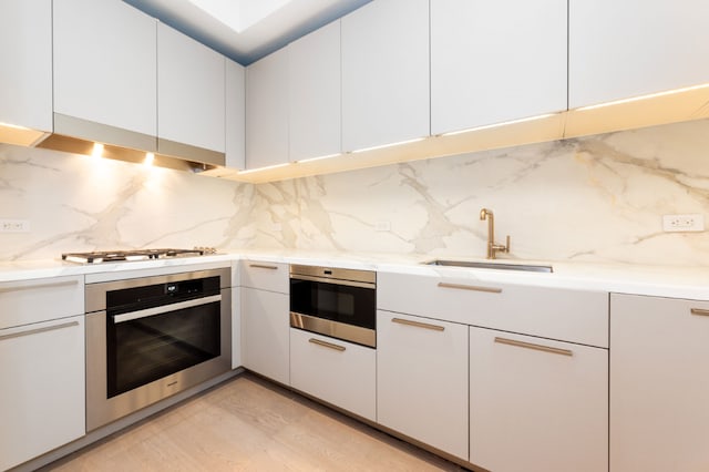 kitchen featuring stainless steel appliances, decorative backsplash, white cabinets, light hardwood / wood-style flooring, and sink