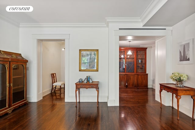 hallway with ornamental molding, visible vents, baseboards, and wood finished floors