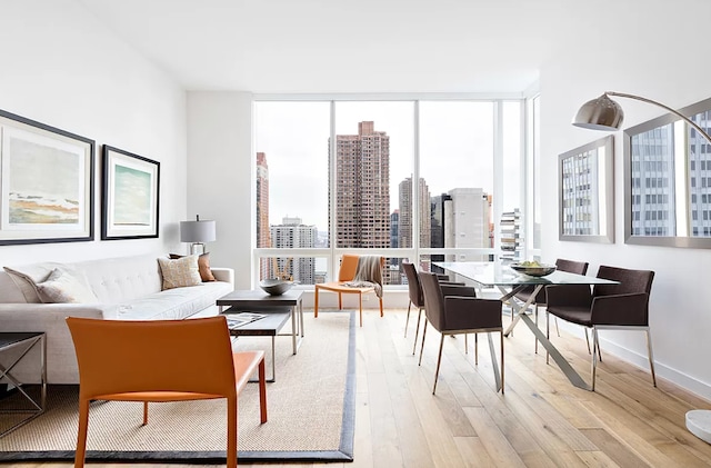 dining area featuring light wood finished floors, floor to ceiling windows, a city view, and a healthy amount of sunlight