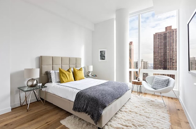 bedroom with a view of city, baseboards, a wall of windows, and light wood-type flooring
