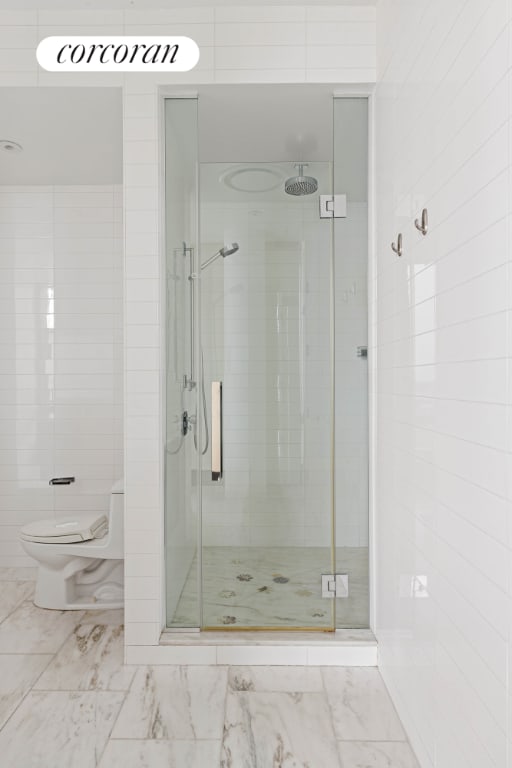 bathroom with toilet, a shower with door, and tile walls