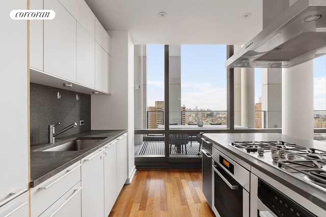 kitchen featuring sink, gas stovetop, white cabinets, wall chimney exhaust hood, and light wood-type flooring