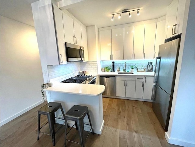 kitchen featuring kitchen peninsula, sink, appliances with stainless steel finishes, white cabinets, and a kitchen bar