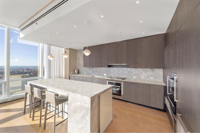 kitchen with a center island, pendant lighting, a wall of windows, stainless steel appliances, and decorative backsplash