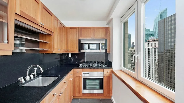 kitchen with sink, appliances with stainless steel finishes, tile patterned flooring, dark stone countertops, and tasteful backsplash