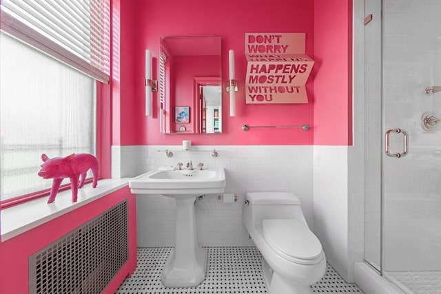 bathroom with toilet, a shower with door, tile walls, and a wealth of natural light