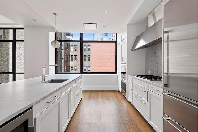 kitchen with appliances with stainless steel finishes, a sink, baseboards, beverage cooler, and light wood-style floors