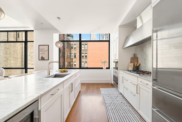 kitchen featuring wood finished floors, wall chimney range hood, white cabinetry, a sink, and stainless steel appliances