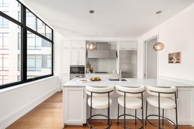 10 Madison Sq W Unit 10A, New York City, NY 10010 - kitchen featuring built in appliances, wall chimney exhaust hood, white cabinets, a sink, and a kitchen bar