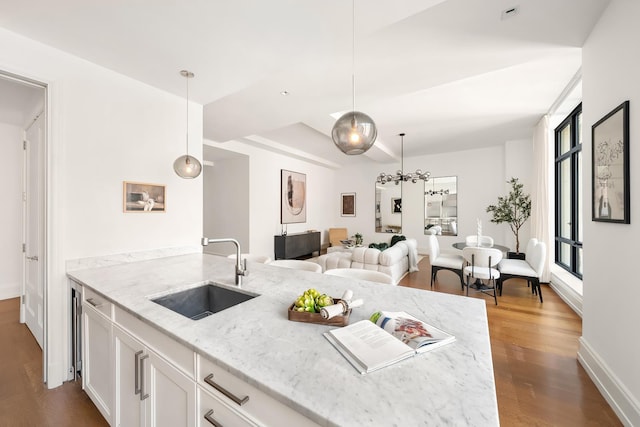 kitchen featuring pendant lighting, dark wood-style flooring, light stone countertops, white cabinets, and a sink
