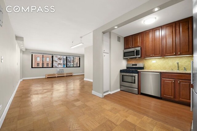 kitchen featuring backsplash, baseboards, open floor plan, stainless steel appliances, and a sink