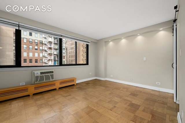 spare room with a baseboard heating unit, an AC wall unit, and baseboards