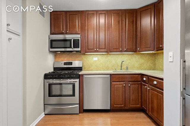 kitchen with a sink, decorative backsplash, light wood-style floors, and stainless steel appliances