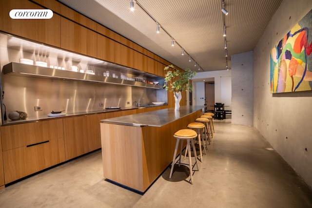 bar featuring rail lighting, sink, and stainless steel counters