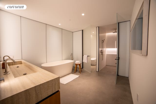 bathroom with vanity, a bath, concrete floors, and toilet