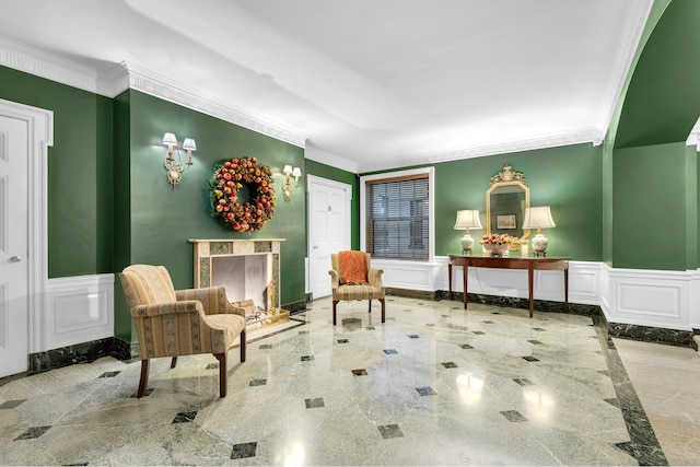 living area featuring a wainscoted wall, a premium fireplace, a decorative wall, and crown molding