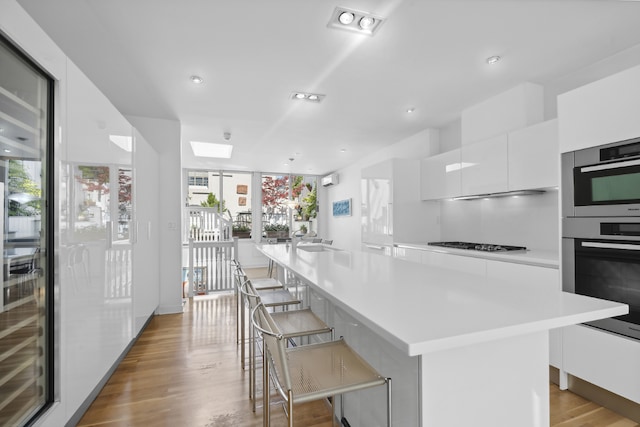 kitchen featuring black gas cooktop, white cabinets, a kitchen bar, light hardwood / wood-style floors, and a center island with sink