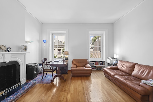 living room with light wood finished floors, ornamental molding, a fireplace with raised hearth, and a wealth of natural light