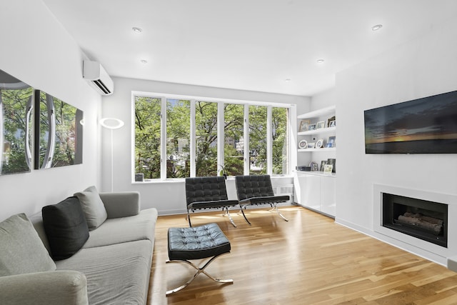 living area featuring plenty of natural light, built in shelves, an AC wall unit, and wood finished floors