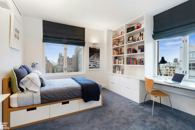 bedroom featuring built in desk, dark carpet, and multiple windows