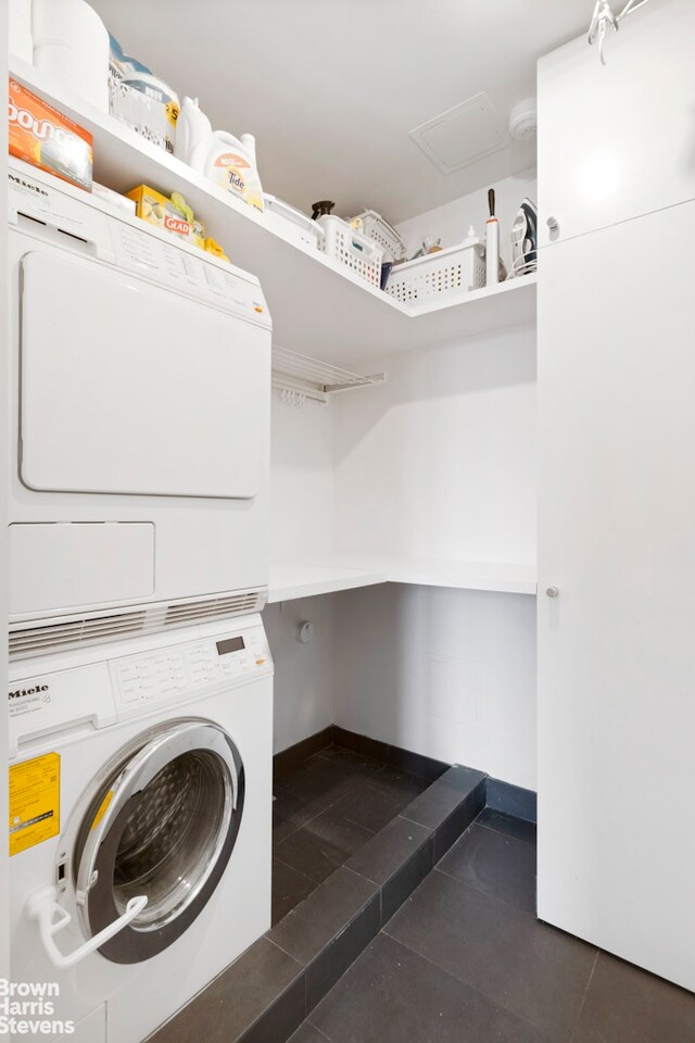 clothes washing area with stacked washer / dryer and dark tile patterned floors