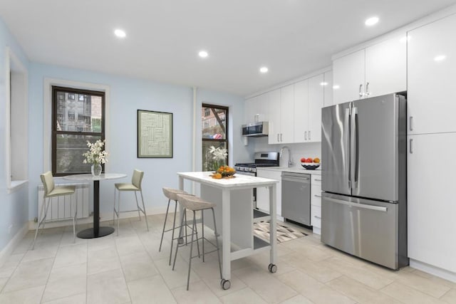 kitchen with white cabinets, radiator heating unit, a kitchen island, a kitchen bar, and stainless steel appliances