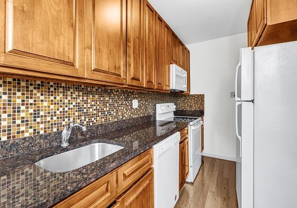 kitchen featuring sink, white appliances, light hardwood / wood-style flooring, dark stone countertops, and tasteful backsplash