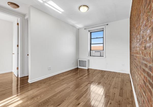 empty room featuring cooling unit, hardwood / wood-style floors, radiator, and brick wall