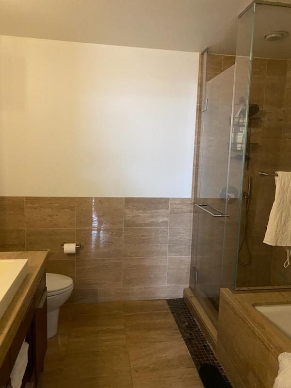 bathroom with tile patterned flooring, toilet, vanity, tile walls, and a stall shower