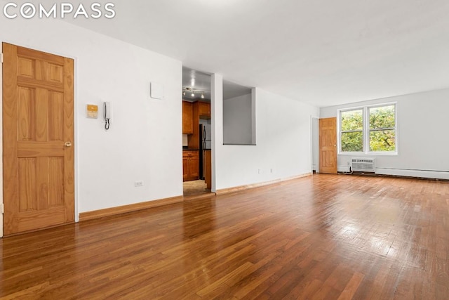 unfurnished living room with hardwood / wood-style flooring, a baseboard radiator, and an AC wall unit