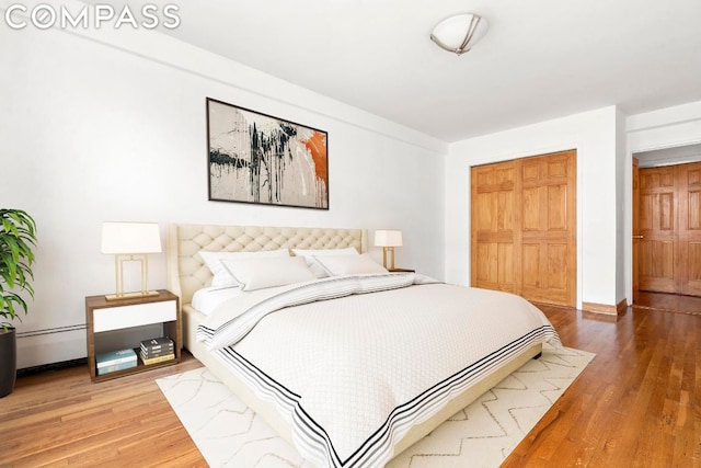 bedroom featuring hardwood / wood-style flooring, a baseboard heating unit, and a closet