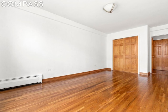 unfurnished bedroom with a baseboard heating unit, a closet, and hardwood / wood-style floors