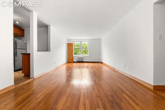 unfurnished living room featuring light wood-type flooring, a wall unit AC, and a baseboard heating unit