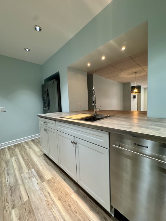 kitchen with pendant lighting, wood counters, white cabinets, stainless steel appliances, and light hardwood / wood-style flooring