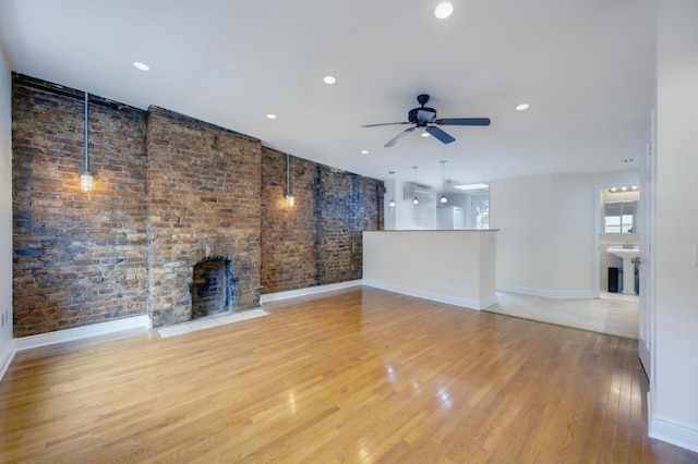 unfurnished living room with ceiling fan, brick wall, a fireplace, and light hardwood / wood-style floors