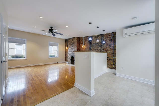 unfurnished living room with ceiling fan, brick wall, a wall unit AC, and light hardwood / wood-style flooring