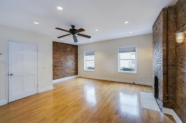 unfurnished living room featuring ceiling fan, a large fireplace, brick wall, and light hardwood / wood-style floors