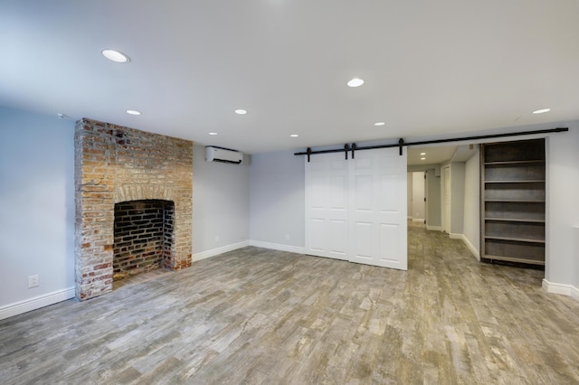 unfurnished living room with a barn door, a wall mounted AC, a brick fireplace, and light hardwood / wood-style flooring